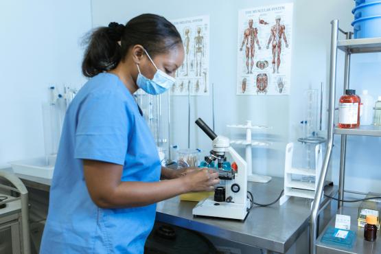 Black nurse looking at a microscope in a laboratory