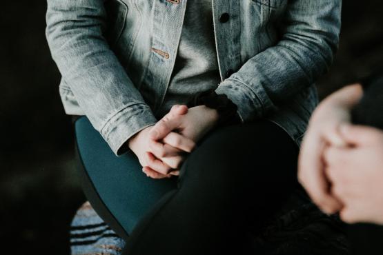 Two people sitting in a dark room talking each with their hands clasped together