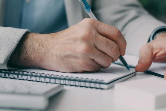 Person writing in notebook with only hands and arms visible