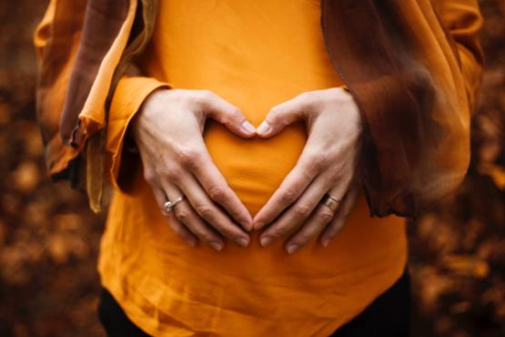 Pregnant woman in orange top with hands forming a heart