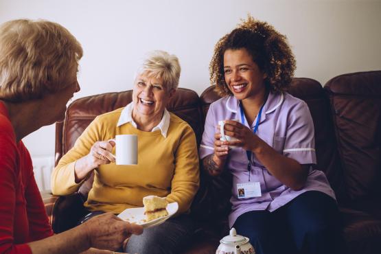 Two older women in a care home laughing with their nurse