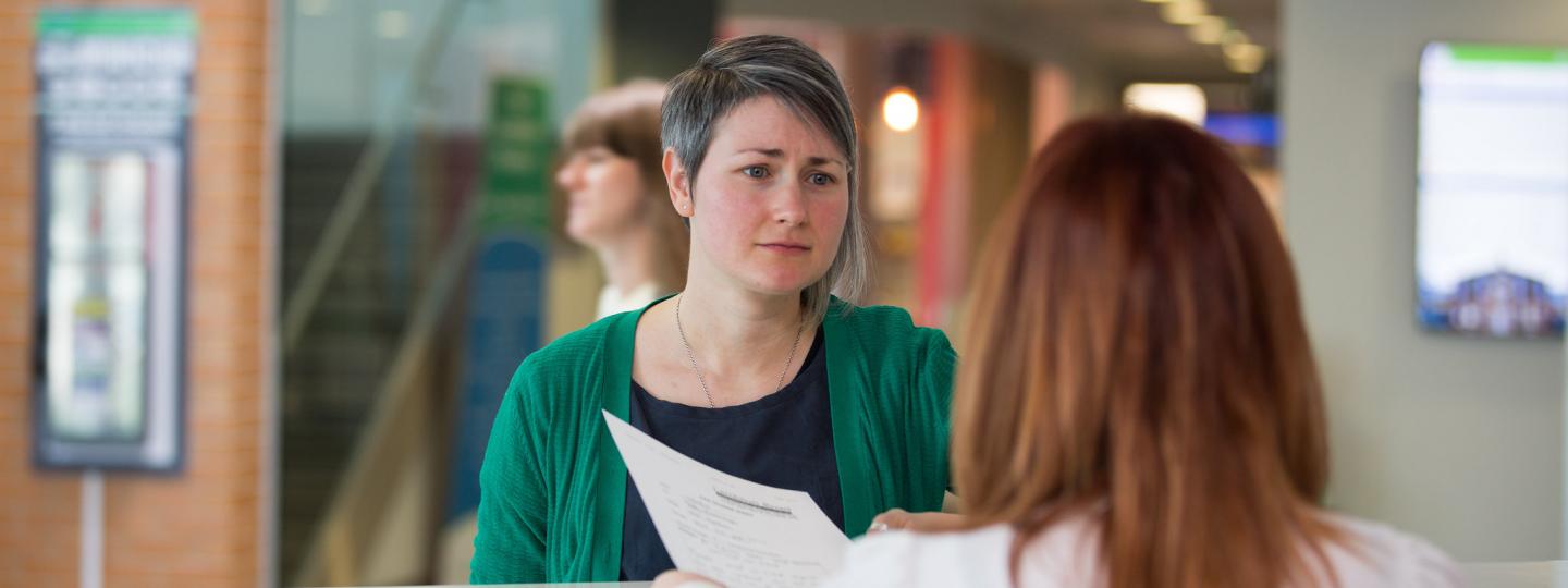 Woman talking to a receptionist about some paperwork in a hospital