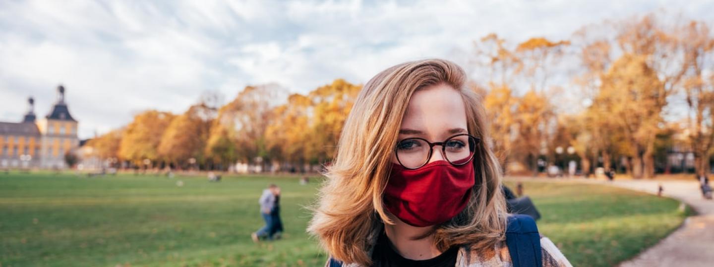 Woman stood in an open field wearing a winter coat and a mask