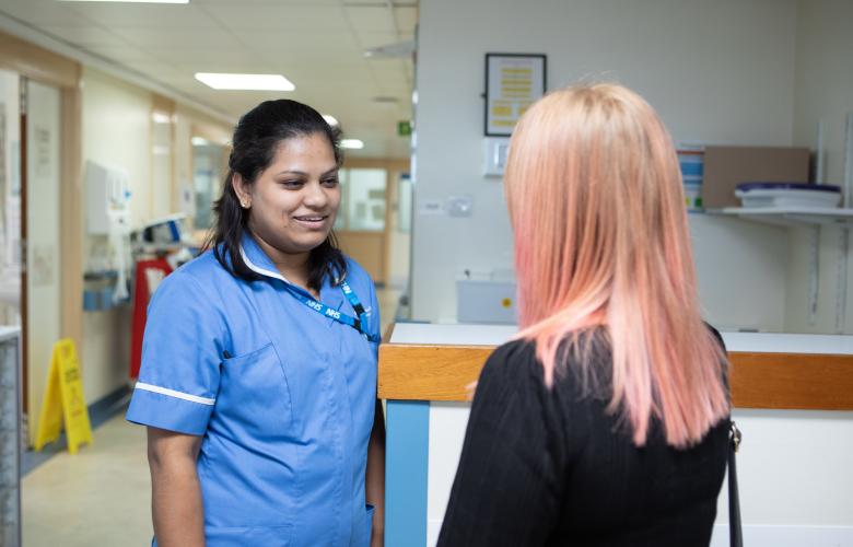 Nurse talking to a woman with pink hair in a hospital corridor