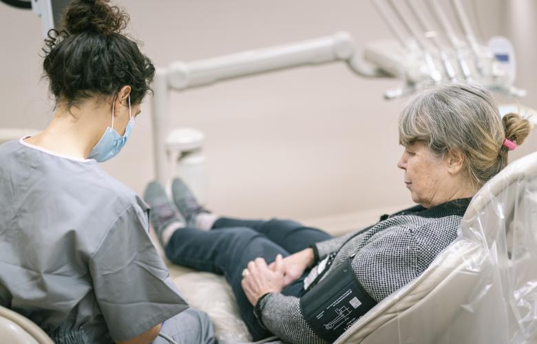 Woman sitting in a dentist's chair having her blood pressure taken by a dentist