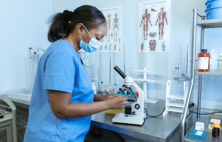 Black nurse looking at a microscope in a laboratory