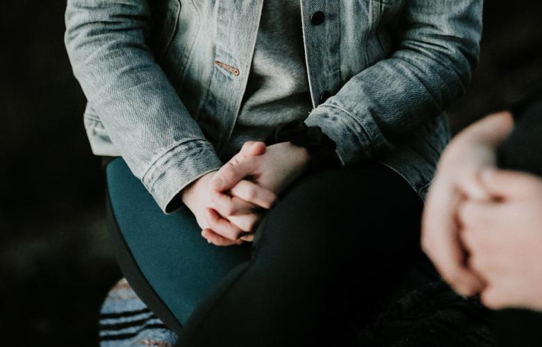 Two people sitting in a dark room talking each with their hands clasped together