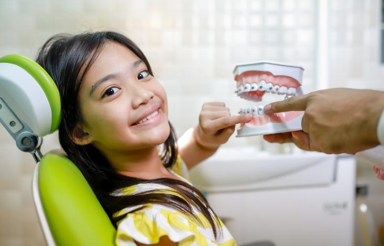 Young Asian girl in a dentist chair with her finger touching a mould of teeth and mouth
