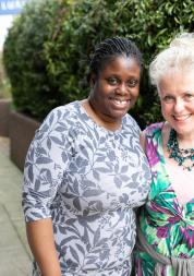 Two women stood in a courtyard with their arms round each other