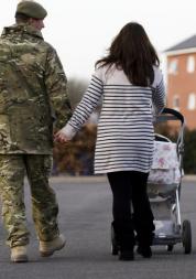 Rear view of a male soldier in uniform walking with a lady pushing a buggy