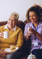 Two older women in a care home laughing with their nurse